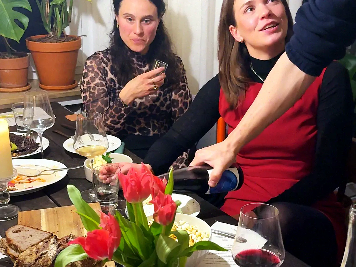 Gäste an einer gedeckten Tafel, es wird Wein eingeschenkt