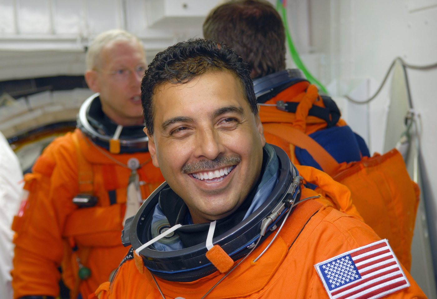 Der Astronaut José Hernández im orangefarbenen Startanzug, lächelnd kurz vor dem Einstieg in die Raumfähre Discovery, August 2009